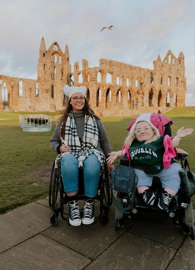 Two women, both using wheelchairs, explore a heritage abbey building.